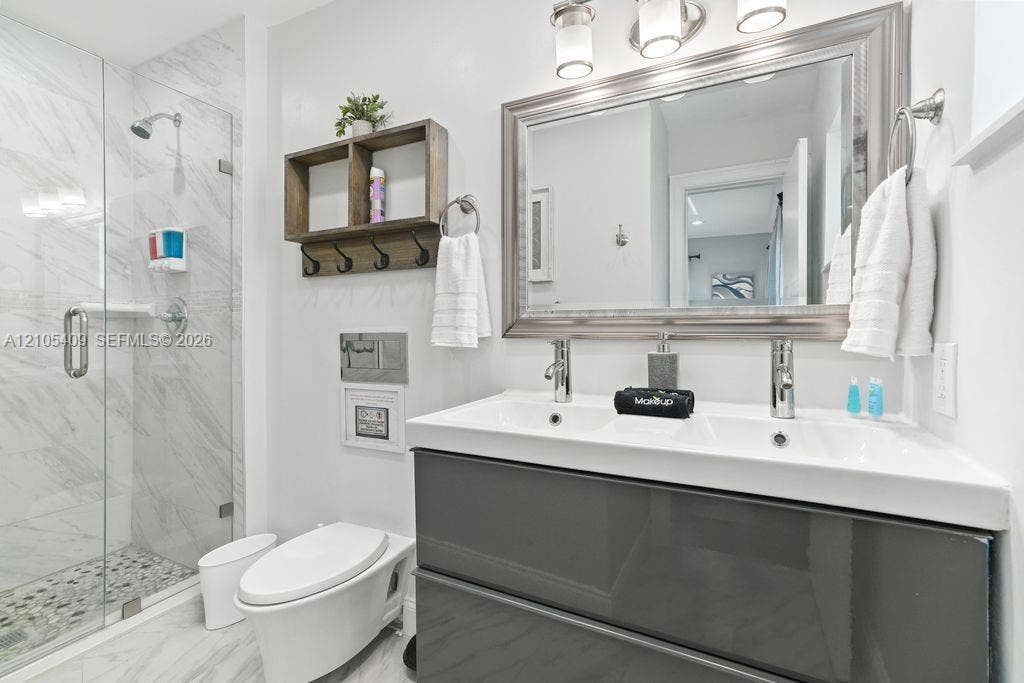 Glass-enclosed shower with white marble-look tile and pebble-style floor