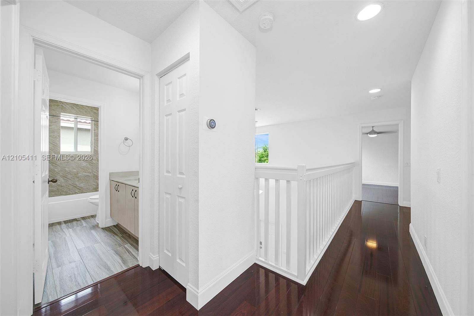 Hallway featuring dark wood-finish flooring, white baluster railing, and recessed lighting