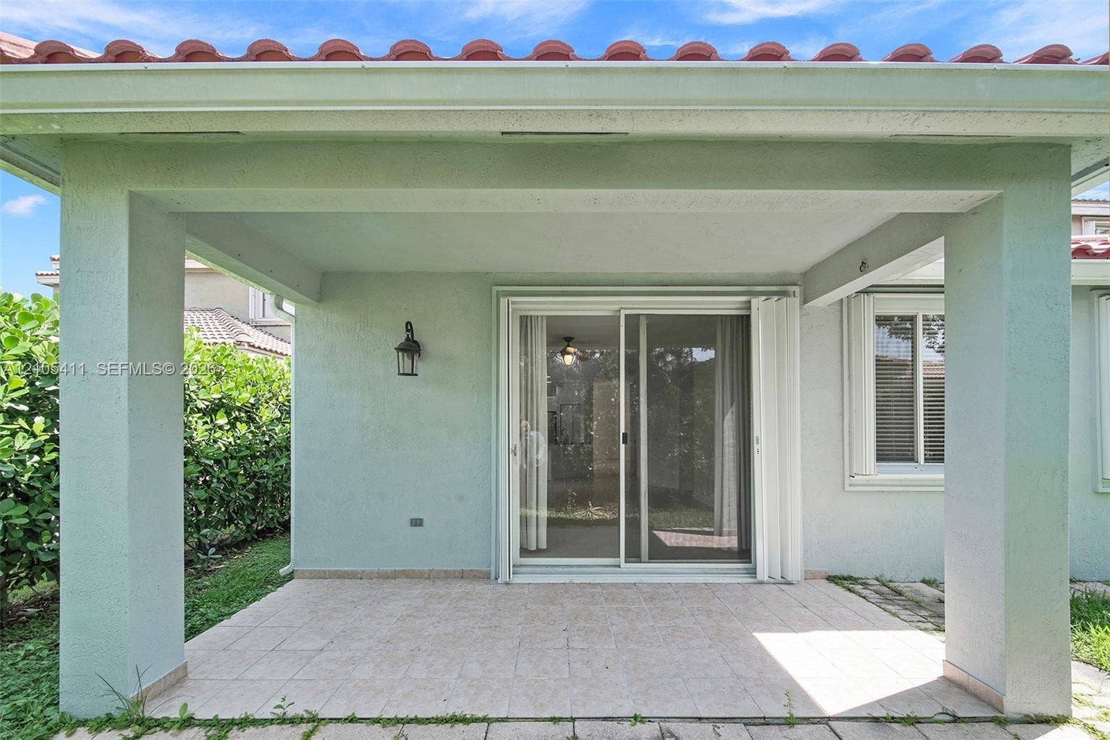 Covered patio with tile flooring, sliding glass door, and exterior wall-mounted lighting