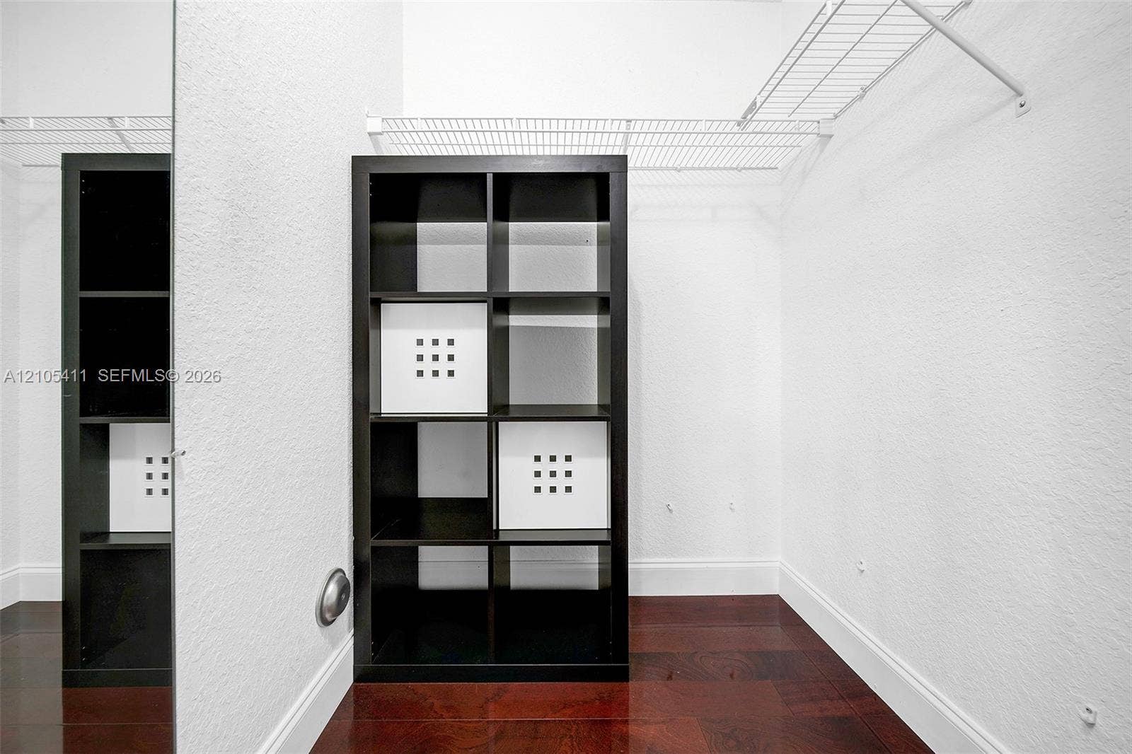 Dark wood-finish flooring, white walls, and wire shelving