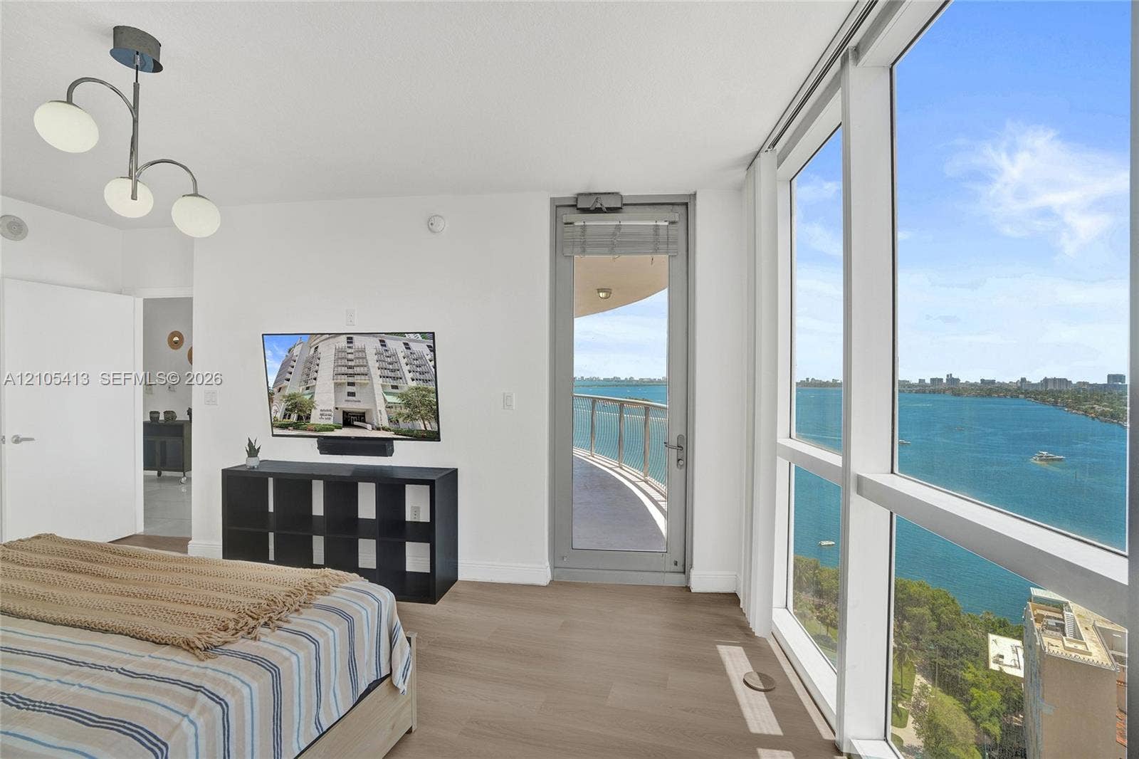 Floor-to-ceiling windows, light wood-finish flooring, balcony access, and modern ceiling lighting