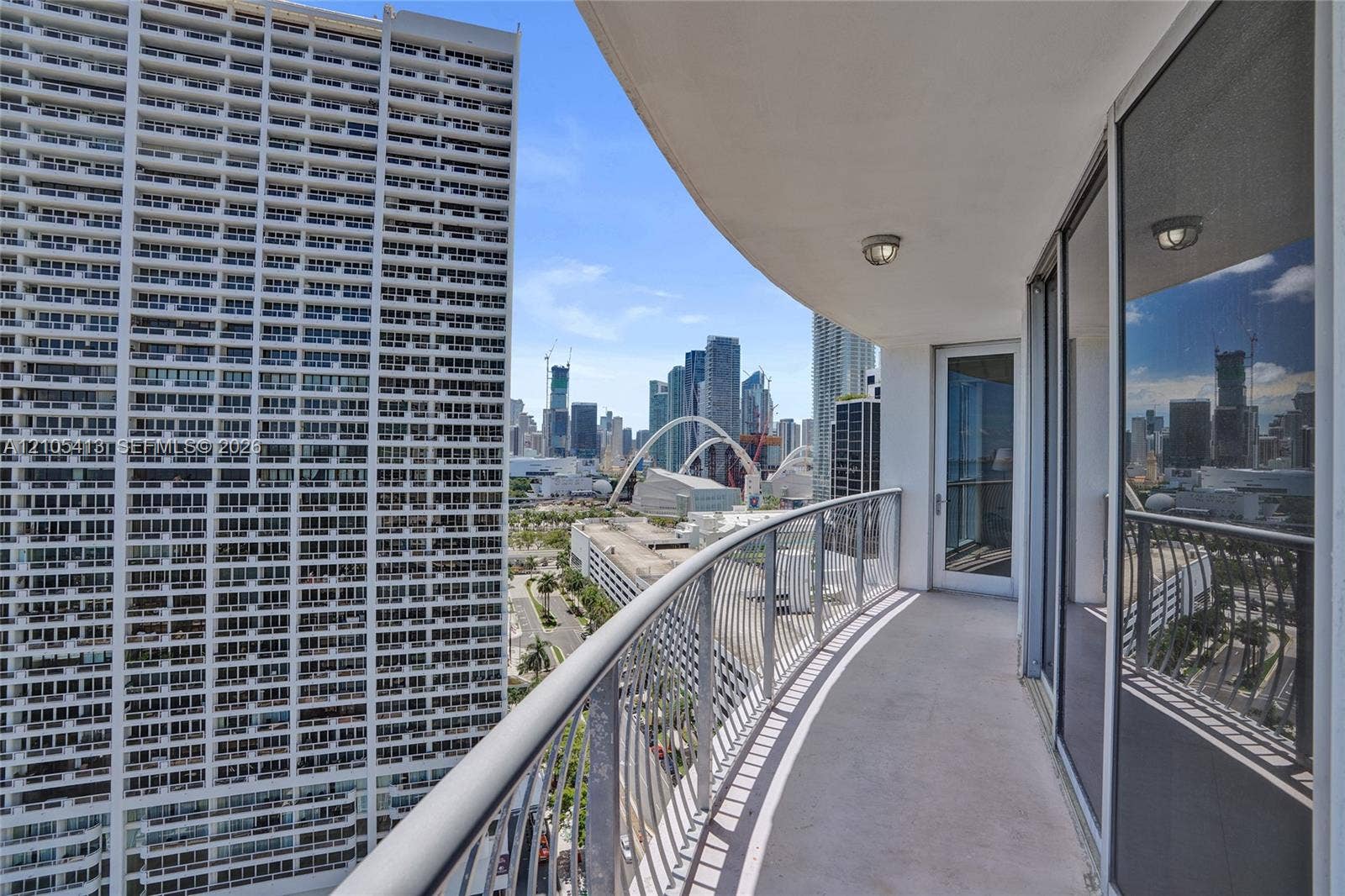 Curved balcony with a metal railing and concrete flooring, featuring two sliding glass doors and recessed lighting