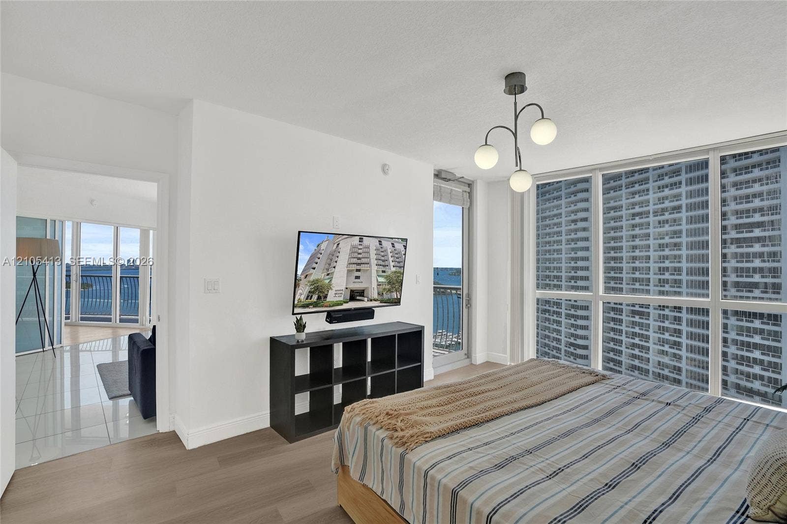 Floor-to-ceiling windows, wood-finish flooring, white walls, modern ceiling light fixture, and a glass-paneled balcony