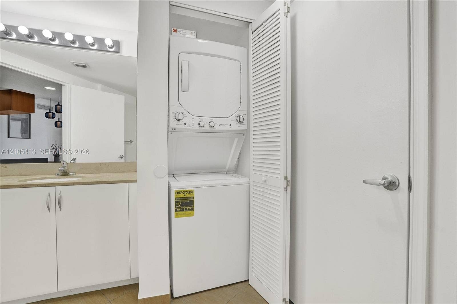 Built-in stacked washer and dryer, vanity with a rectangular sink, wall-mounted light fixture, and white cabinet storage