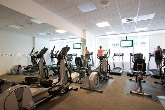 Fitness center with mirrored wall, multiple cardio machines, mounted flat-screen displays, and recessed lighting