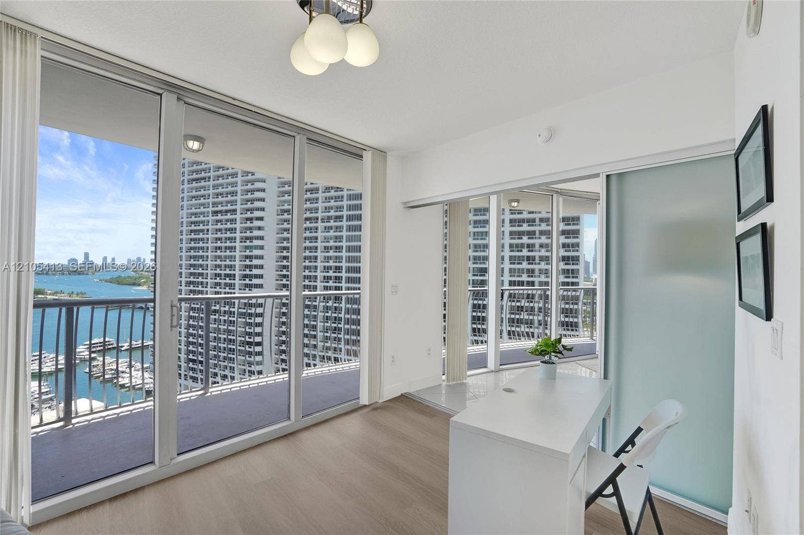 Expansive floor-to-ceiling glass sliding doors, private balcony with metal railings, wood-finish flooring, built-in counter surface, and a frosted glass sliding door