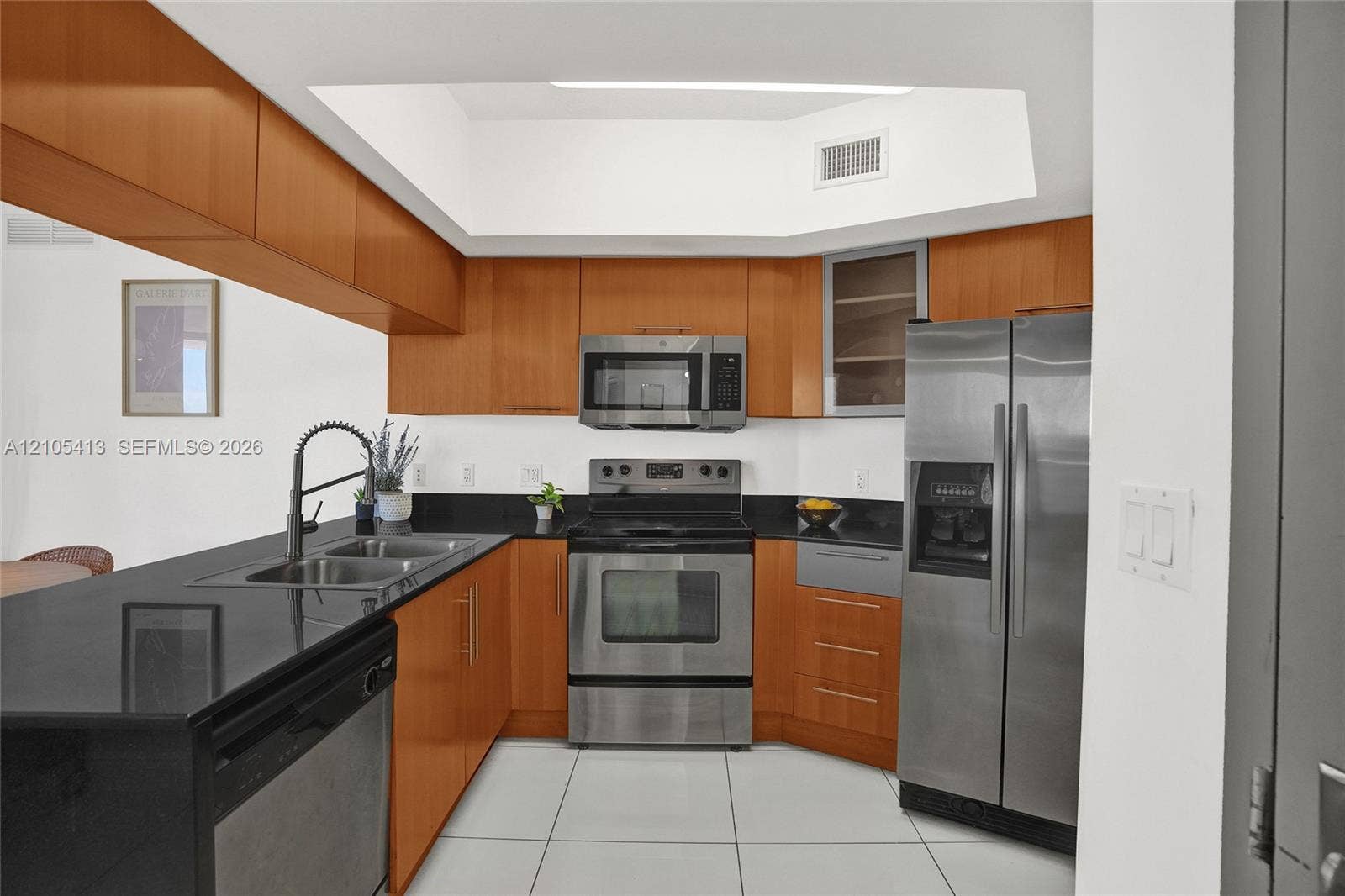 Kitchen featuring wood cabinetry, black countertops, stainless steel appliances, and white tile flooring