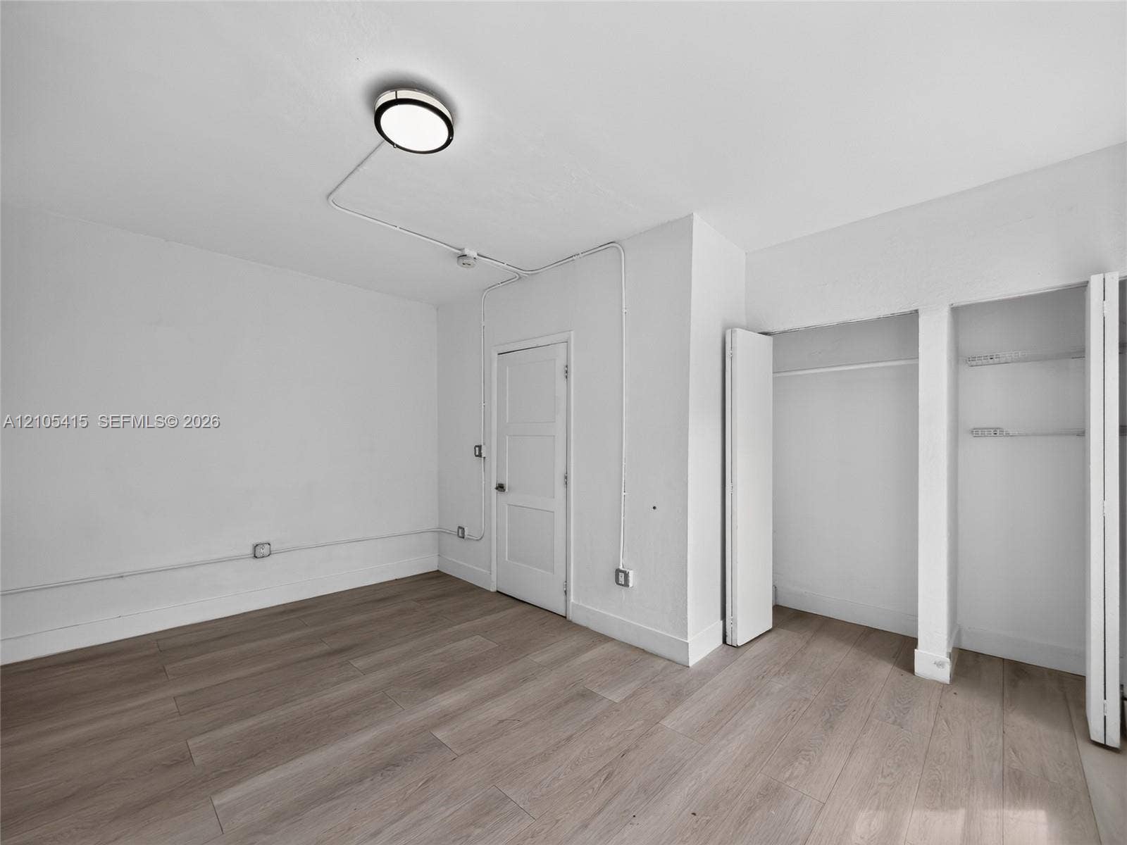 967 SW 5th Street, #11, Miami, Miami, FL 33130 Wood-finish flooring, dual-closet storage with shelving, three-panel interior door, and surface-mounted industrial-style lighting