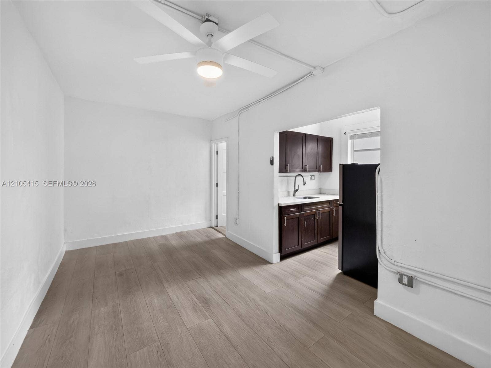 967 SW 5th Street, #11, Miami, Miami, FL 33130 Interior space featuring wood-finish flooring, a white ceiling fan with integrated lighting, and a kitchenette equipped with dark-finish cabinetry, solid-surface countertops, and a single-basin sink