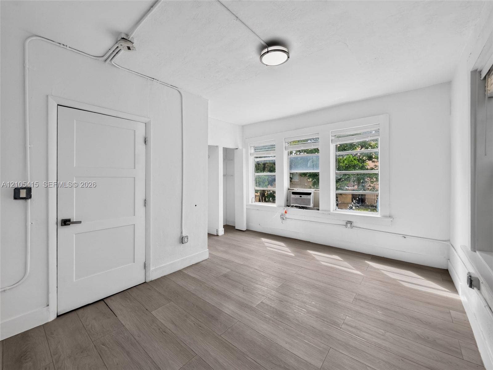 967 SW 5th Street, #11, Miami, Miami, FL 33130 Neutral-toned wood-finish flooring, three paneled windows with natural light, a white three-panel door with modern hardware, and flush-mount ceiling lighting