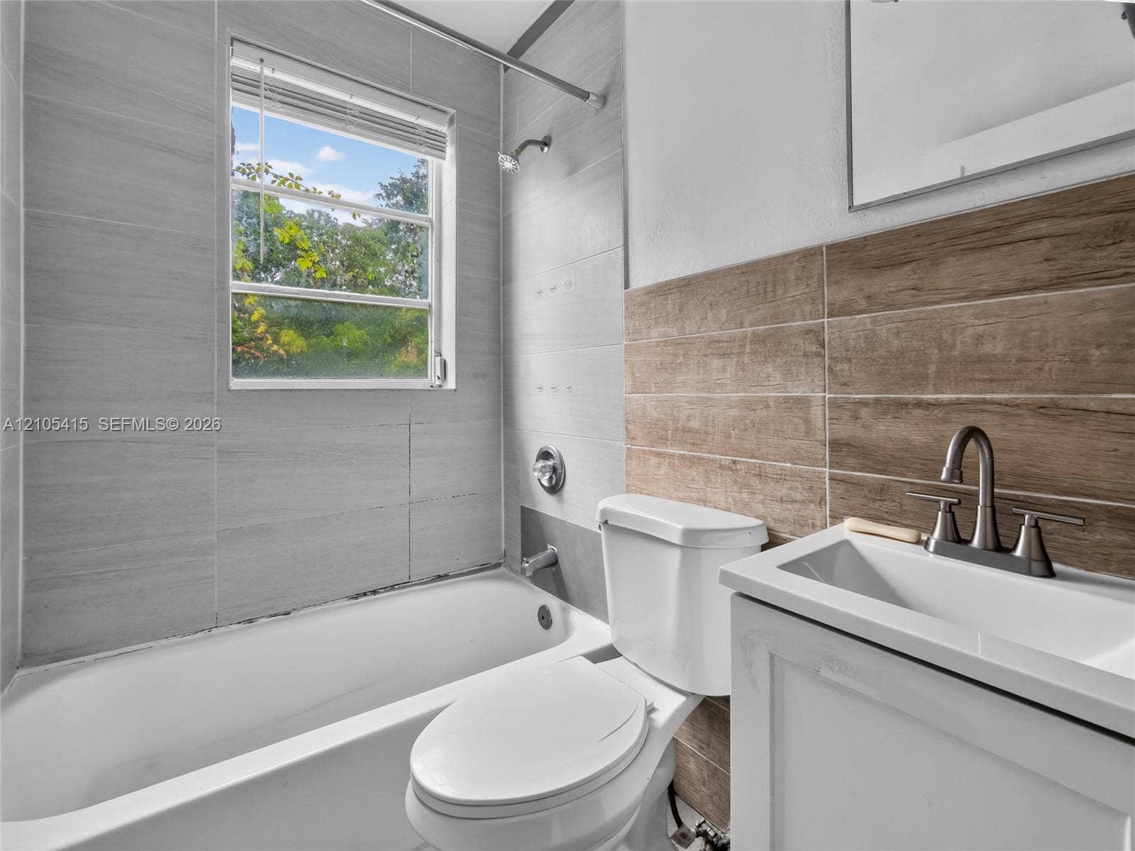 967 SW 5th Street, #11, Miami, Miami, FL 33130 Bathroom featuring grey wall tile, wood-finish tile accents, a porcelain tub with shower head, and a white vanity with a metal faucet