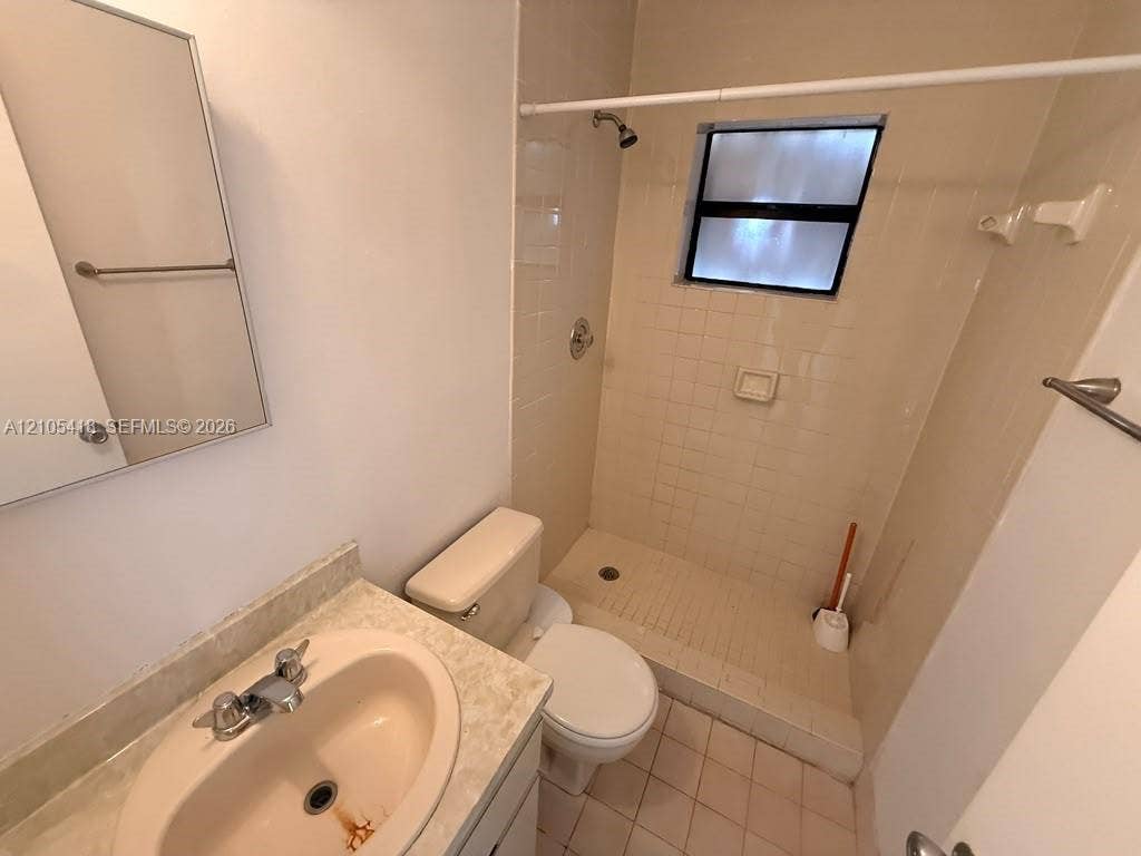 Bathroom featuring a vanity with an integrated sink, a wall-mounted mirror, a tiled shower enclosure, and a window