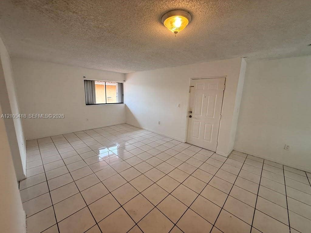 Spacious room featuring white tile flooring, a window with horizontal blinds, and a paneled entry door
