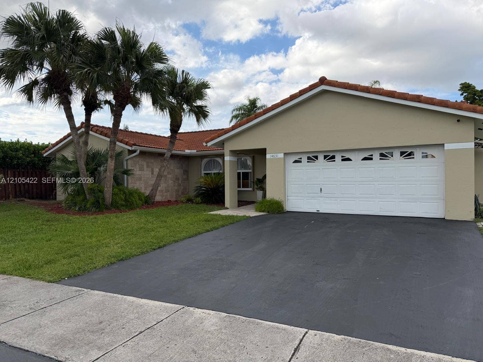 14631 SW 150th Street, Miami, FL 33186 Exterior featuring a terracotta tile roof, beige stucco facade, stone-accented wall, arched window detailing, and a two-car garage
