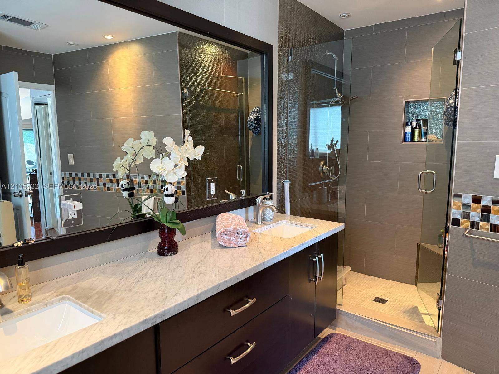 14631 SW 150th Street, Miami, FL 33186 Bathroom featuring a dark wood double vanity with a stone countertop, dual undermount sinks, large framed mirror, and a walk-in glass-enclosed shower with tiled walls and a built-in shower niche