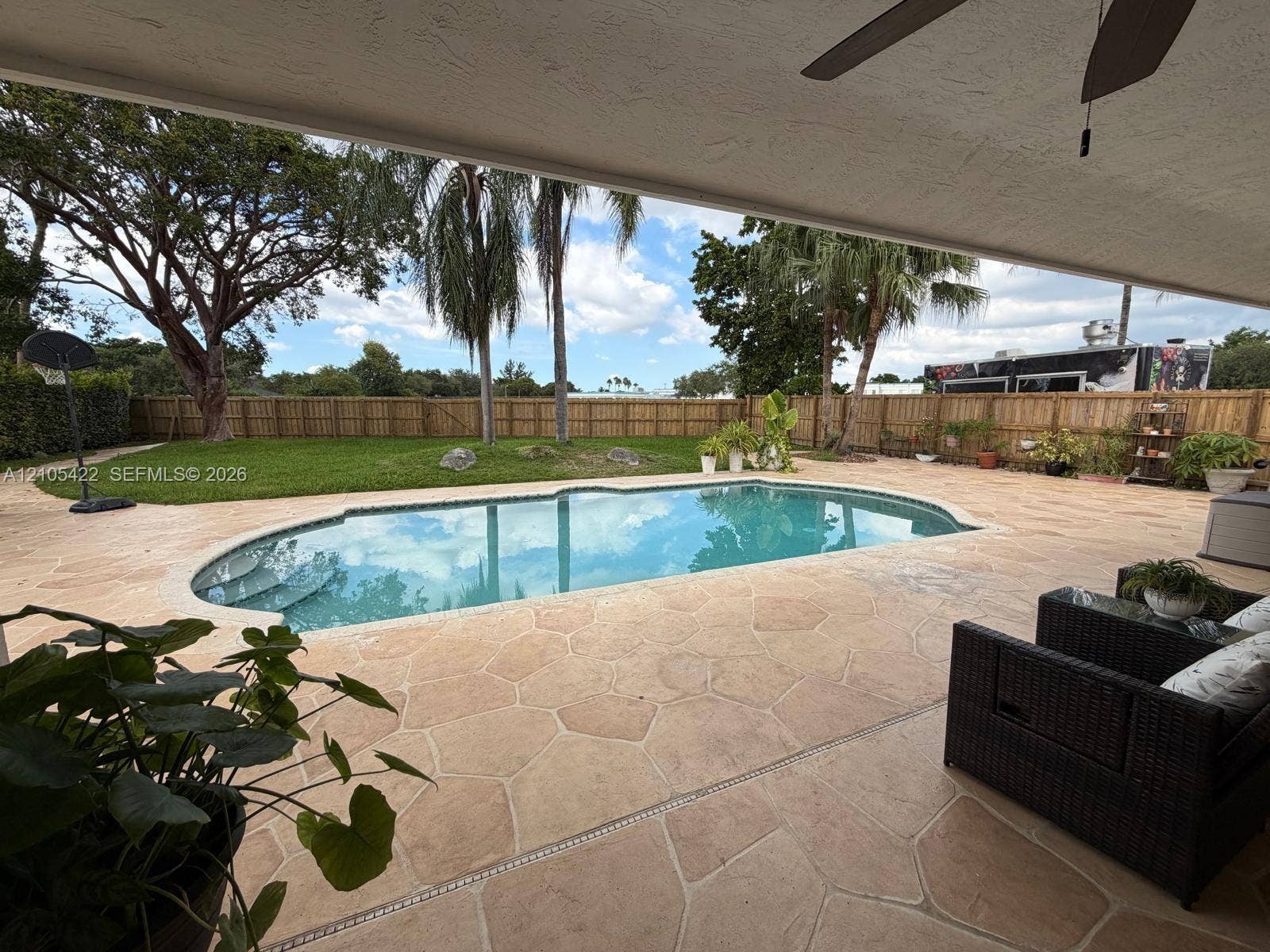14631 SW 150th Street, Miami, FL 33186 Covered patio featuring stone-paver decking, an in-ground swimming pool, manicured lawn, and perimeter wood fencing