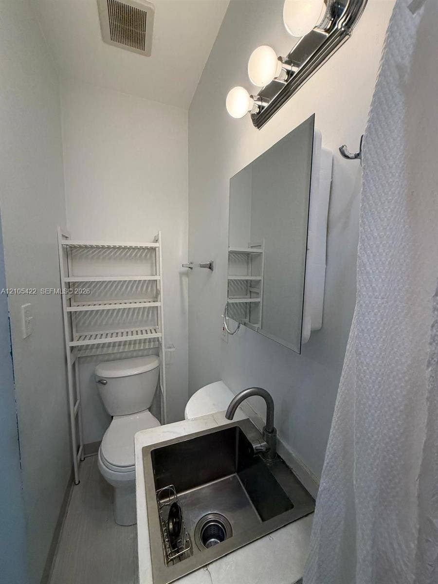 14631 SW 150th Street, Miami, FL 33186 Stainless steel drop-in sink with a high-arch faucet, stone-composite countertop, wall-mounted medicine cabinet, and three-bulb vanity light fixture