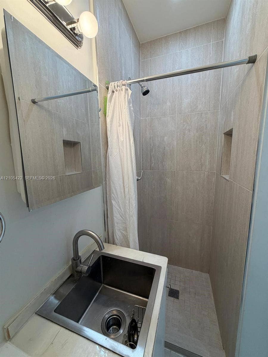 14631 SW 150th Street, Miami, FL 33186 Bathroom featuring a square undermount sink with a gooseneck faucet, light-toned countertop, wall-mounted mirror, and a walk-in shower with neutral wall tiling and recessed shelving
