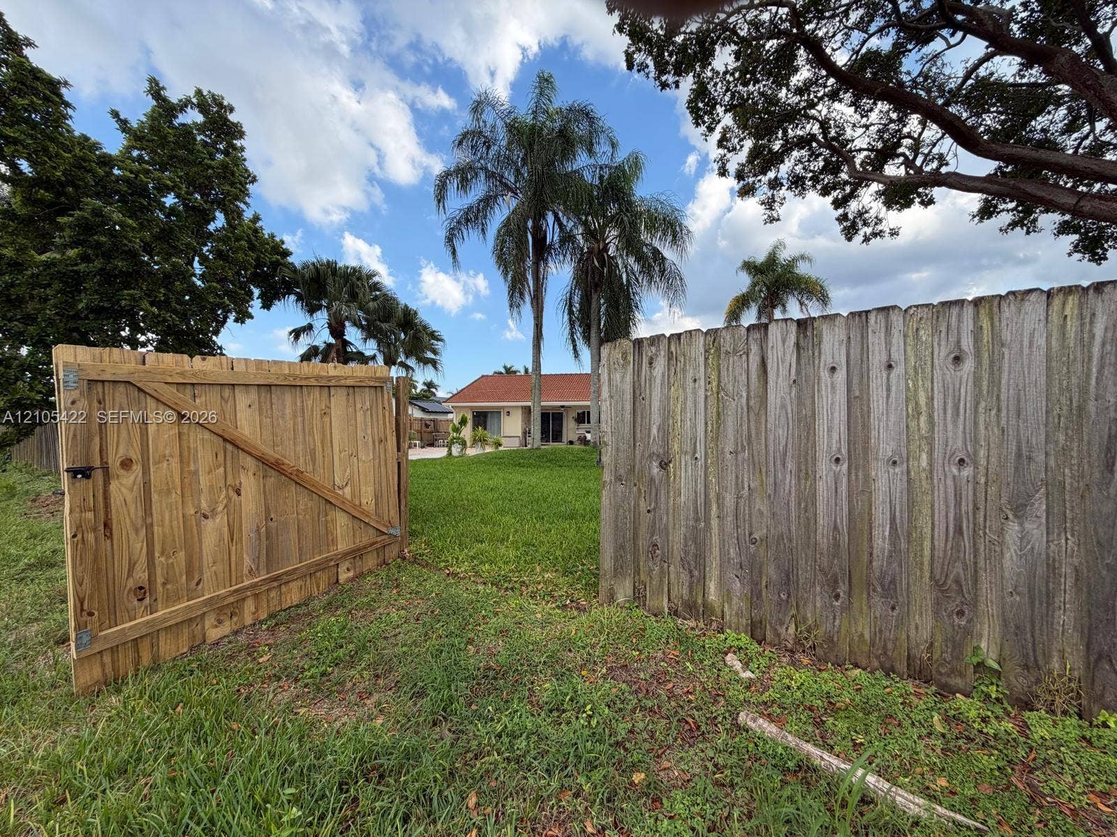 14631 SW 150th Street, Miami, FL 33186 Expansive backyard featuring a wood privacy fence with a gated entry, mature palm trees, and established landscaping