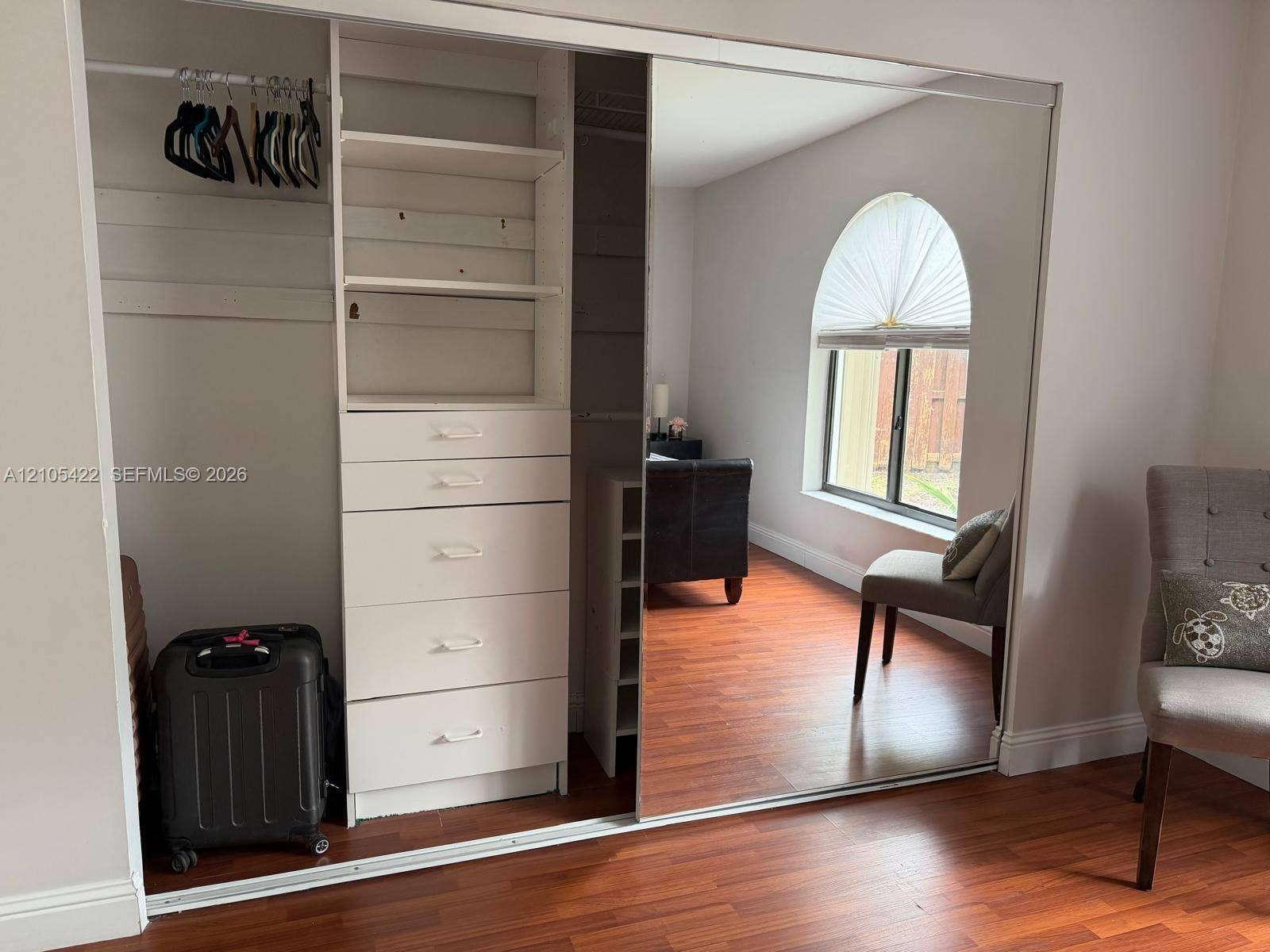 14631 SW 150th Street, Miami, FL 33186 Built-in wardrobe featuring mirrored sliding doors, integrated shelving, and a multi-drawer storage unit, complemented by wood-finish flooring and an arched window