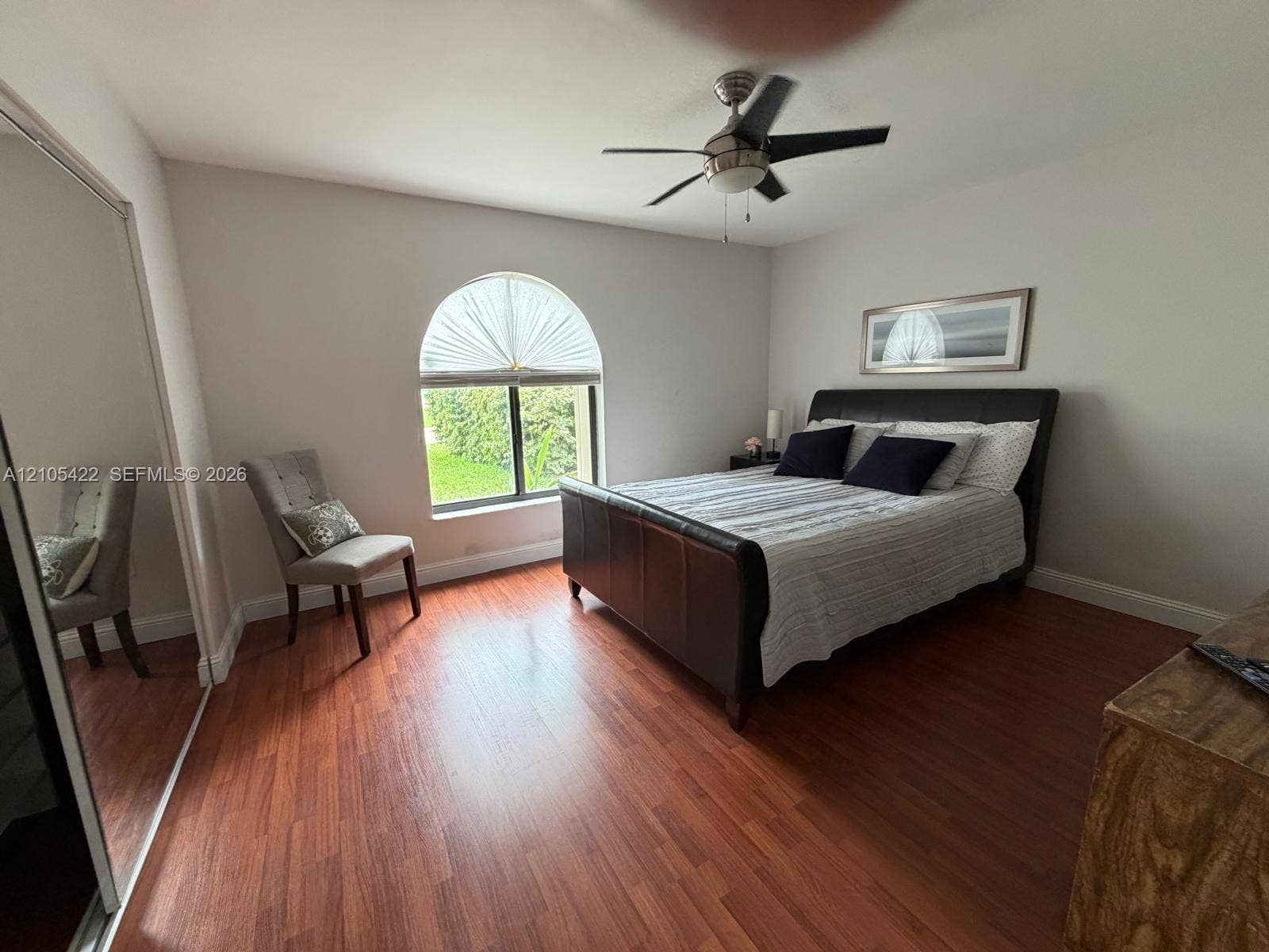 14631 SW 150th Street, Miami, FL 33186 Arched window with decorative fanlight, wood-finish flooring, full-height mirrored sliding closet doors, and ceiling fan with integrated light fixture