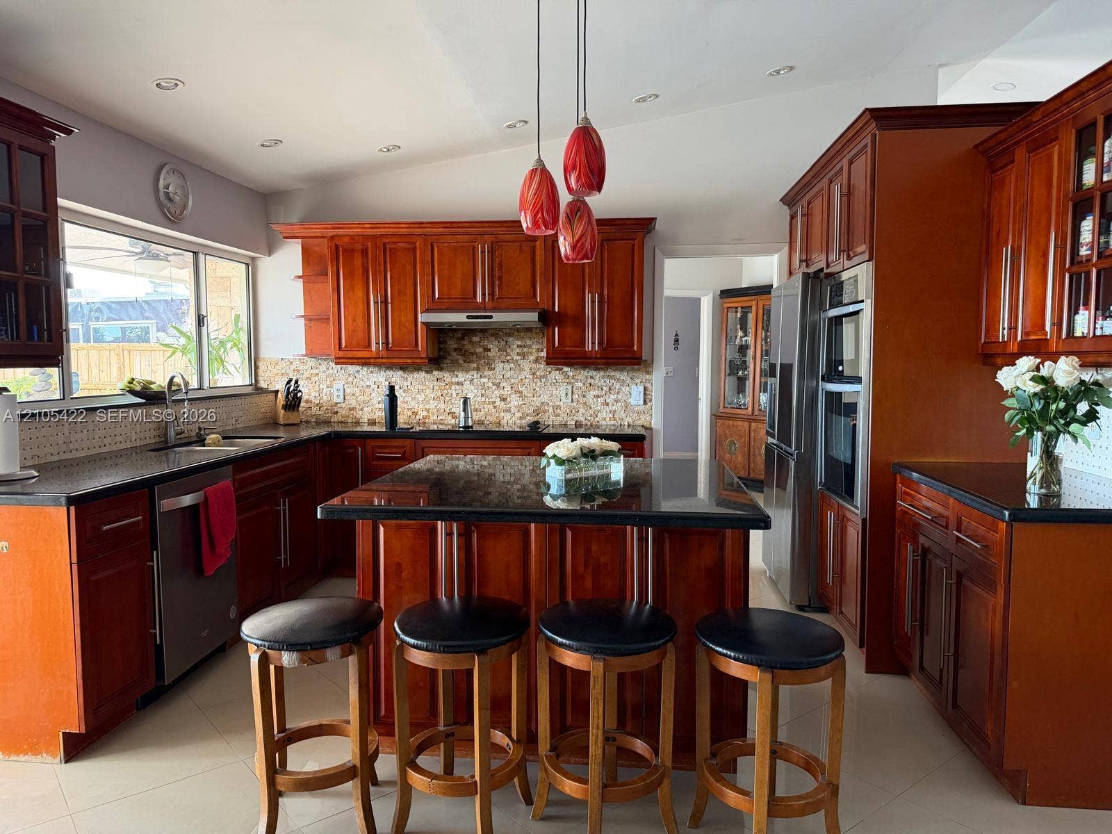 14631 SW 150th Street, Miami, FL 33186 Kitchen featuring cherry-toned cabinetry, dark stone countertops, a multi-tiered glass pendant lighting fixture, a decorative mosaic tile backsplash, and a central island with integrated storage