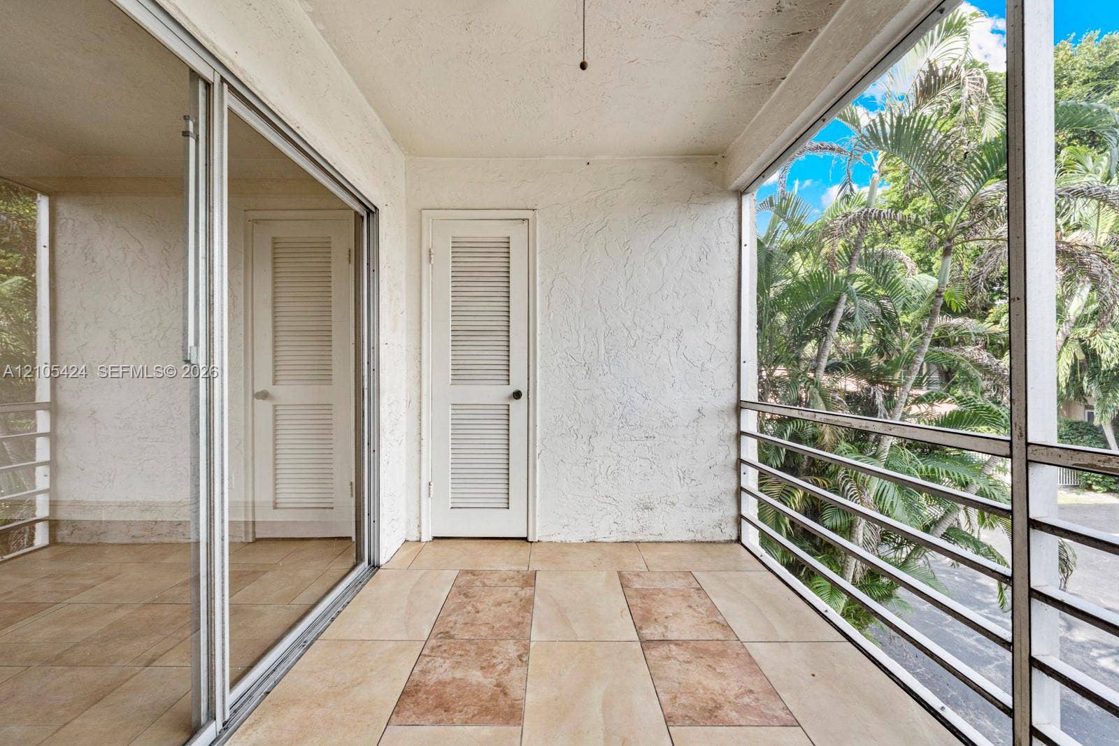 Expansive screened balcony featuring a textured wall finish, tile flooring with patterned accents, and a sliding glass door
