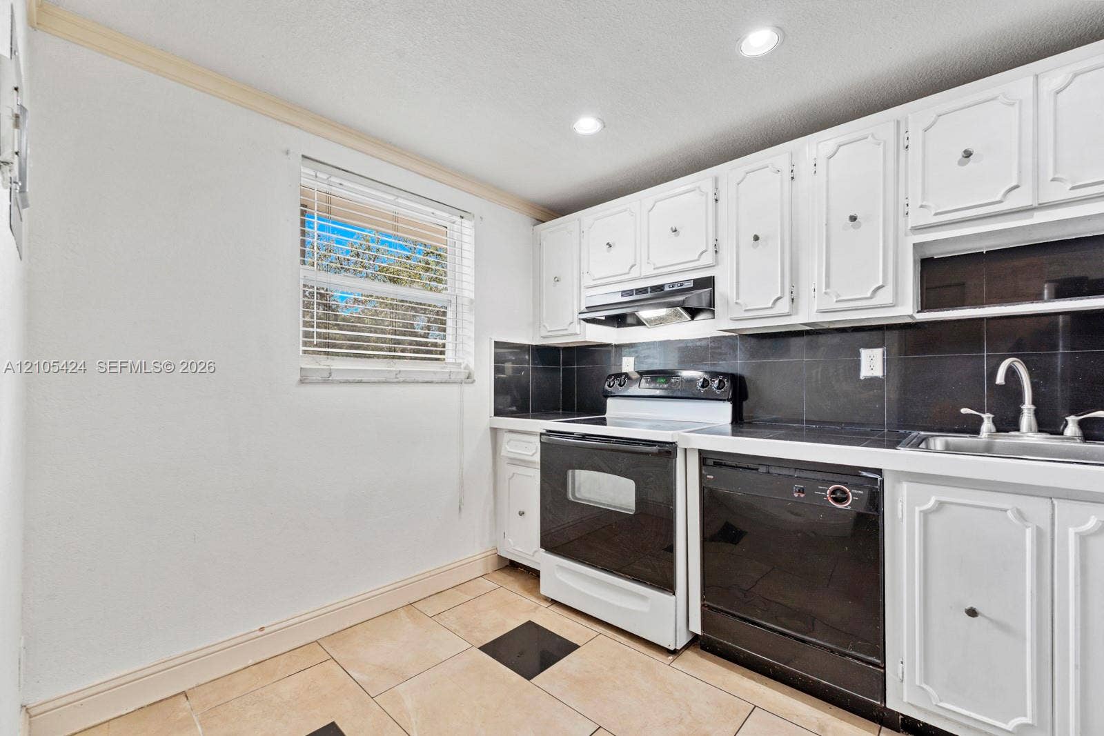 Kitchen featuring white upper and lower cabinetry, black tile backsplash, integrated sink with chrome faucet, and recessed lighting
