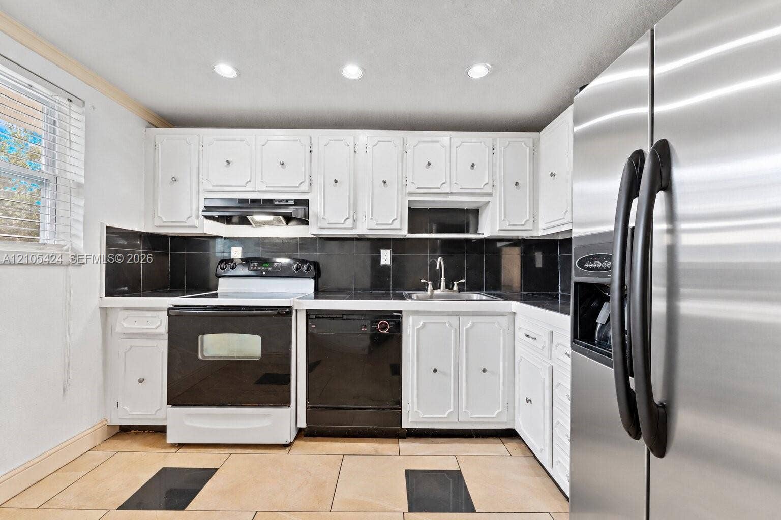 White cabinetry, black tile backsplash, stainless steel refrigerator, black range, and black dishwasher
