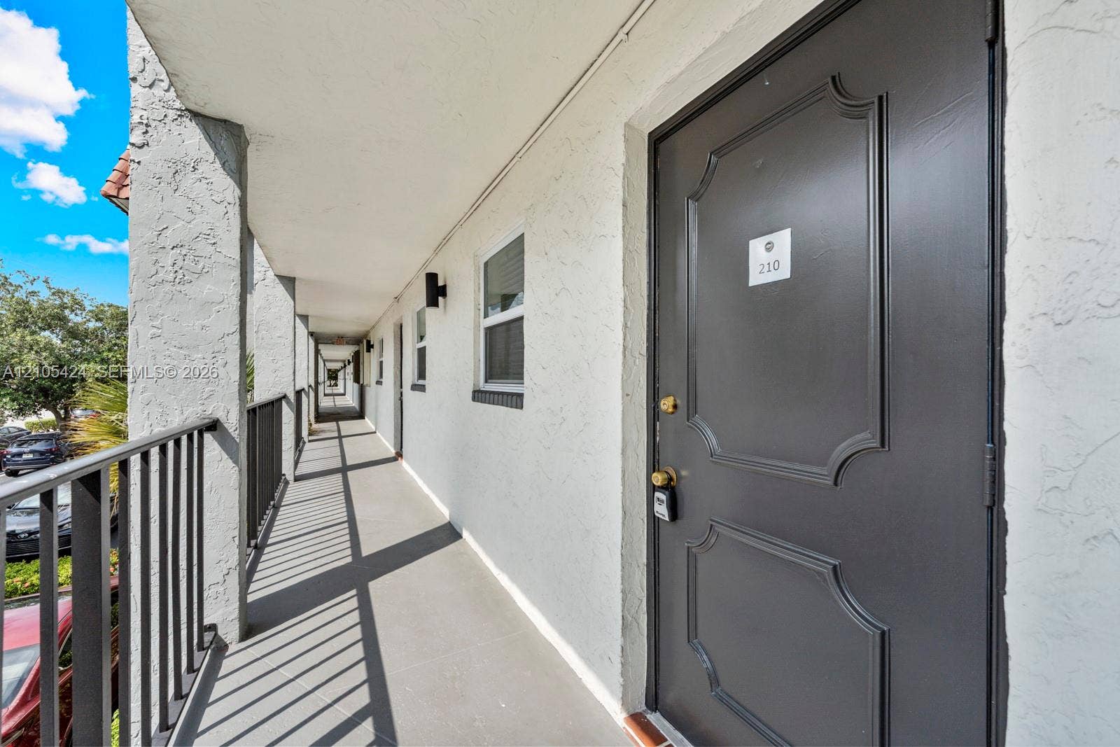 Covered exterior walkway featuring a textured finish, dark gray railing, and exterior lighting fixtures