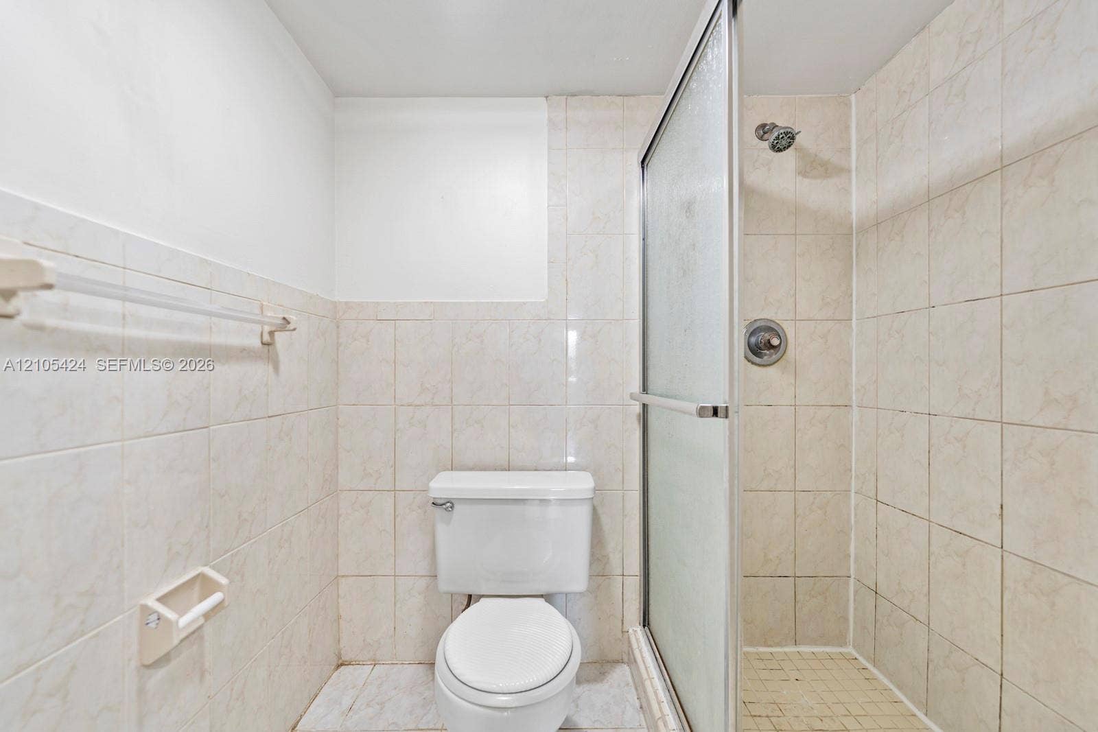 Tiled bathroom featuring a white toilet and a shower with a frosted glass enclosure