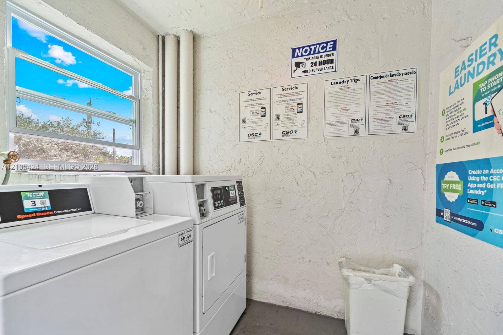 Laundry facility featuring commercial-grade washers and dryers, textured wall finishes, and an exterior-facing window