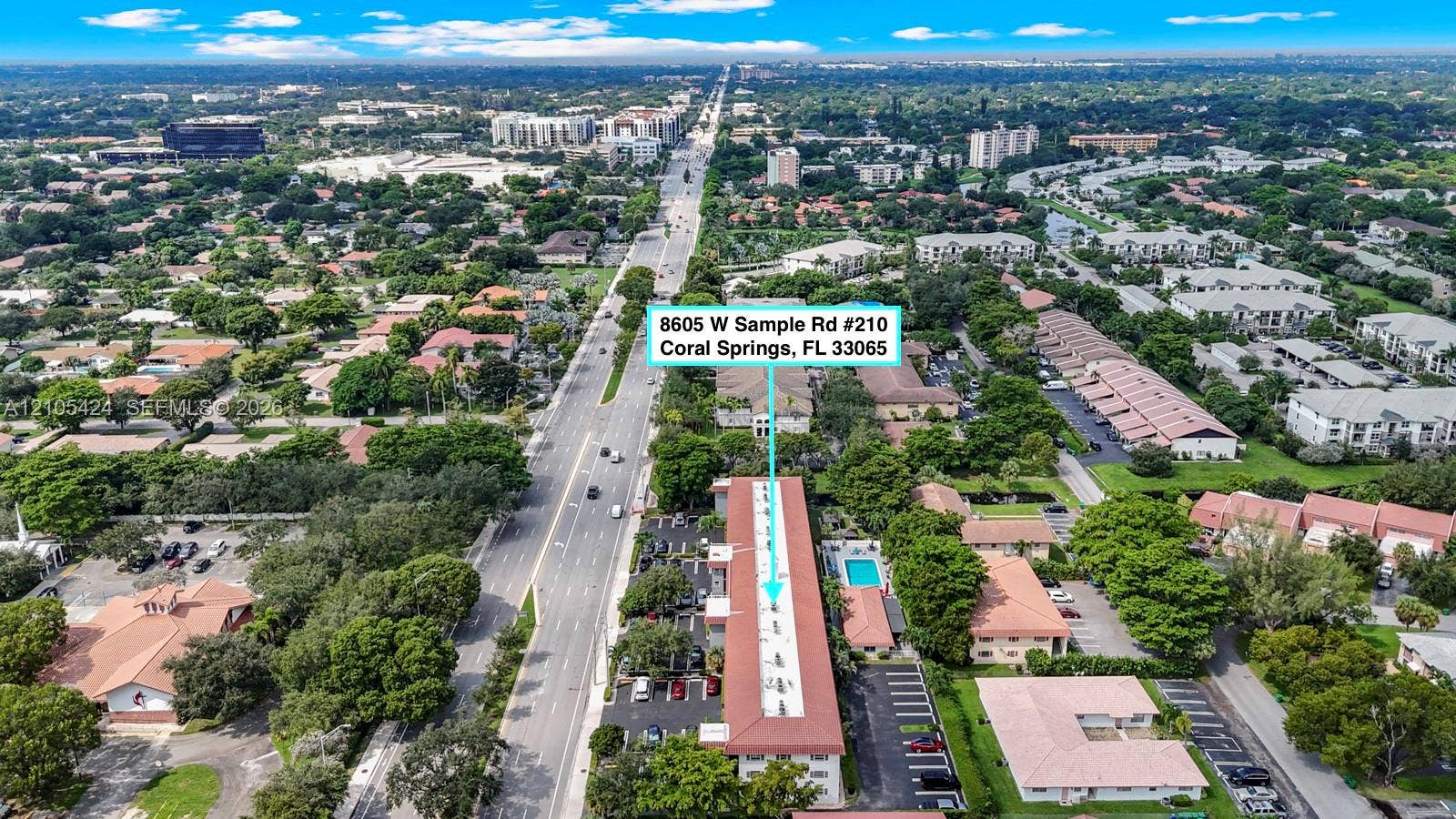 Aerial perspective showcasing a multi-story residential building, an adjacent outdoor swimming pool, and extensive surrounding green spaces