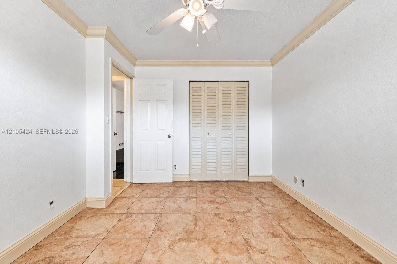 Spacious bedroom featuring ceramic tile flooring, white painted walls, and a tray ceiling with wood trim detailing