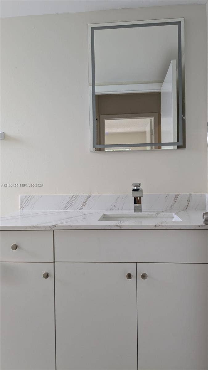 White floating vanity with a polished chrome faucet, rectangular undermount sink, and a framed wall mirror