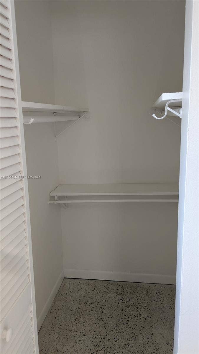 White louvered closet door opening to a closet featuring white walls, white shelving, and a patterned floor