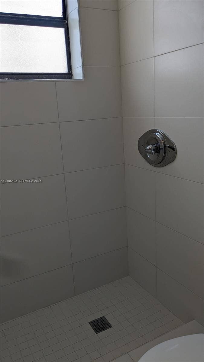 White tiled shower enclosure with a chrome shower control and a small window