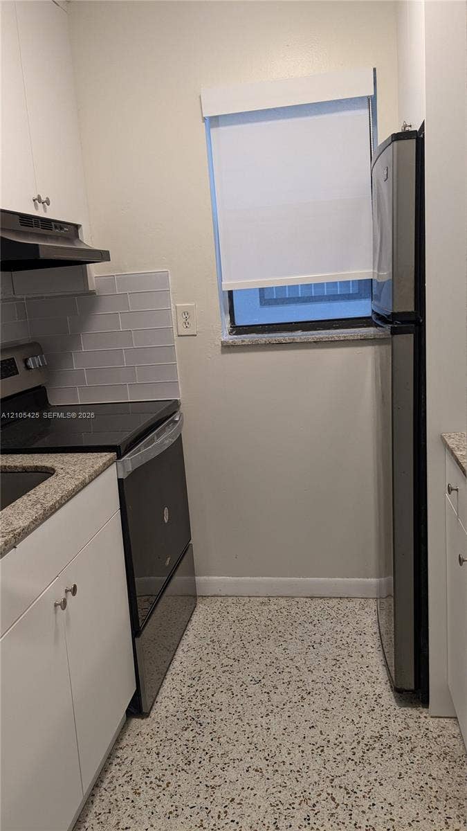 White cabinetry with brushed nickel hardware, granite countertops, tile backsplash, stainless steel appliances, and terrazzo flooring