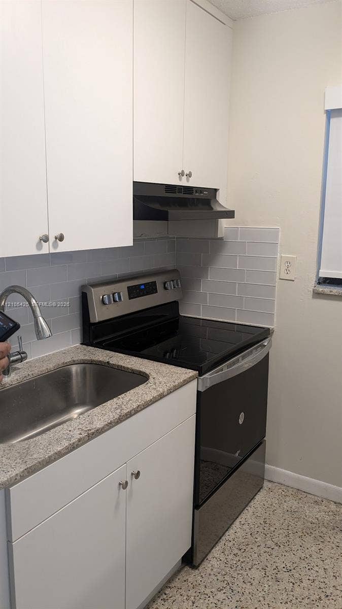 White upper and lower cabinetry, stainless steel sink with a gooseneck faucet, light-toned countertop, and a gray subway tile backsplash
