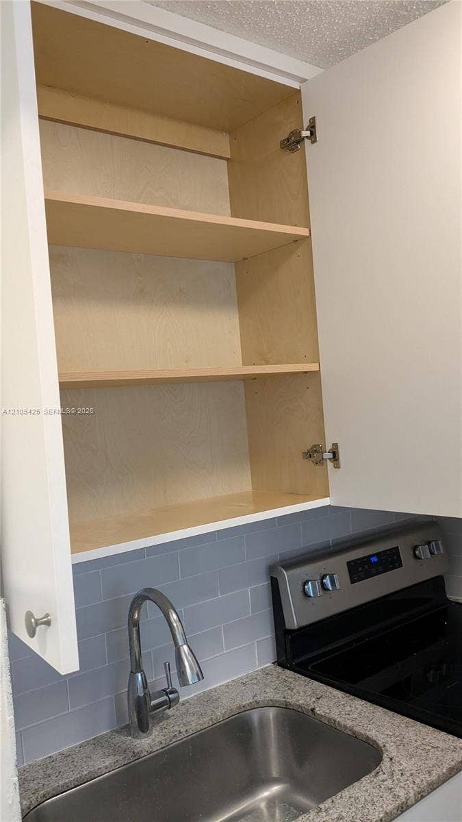 Upper white cabinet with adjustable interior shelving, stainless steel sink, gooseneck faucet, light grey subway tile backsplash, and granite-finish countertop