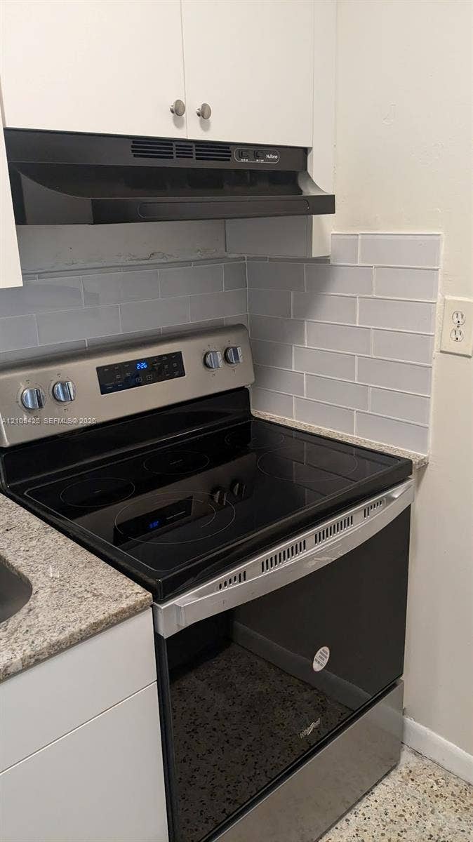 Stainless steel electric range with a smooth cooktop, complemented by light grey subway tile backsplash and a speckled countertop