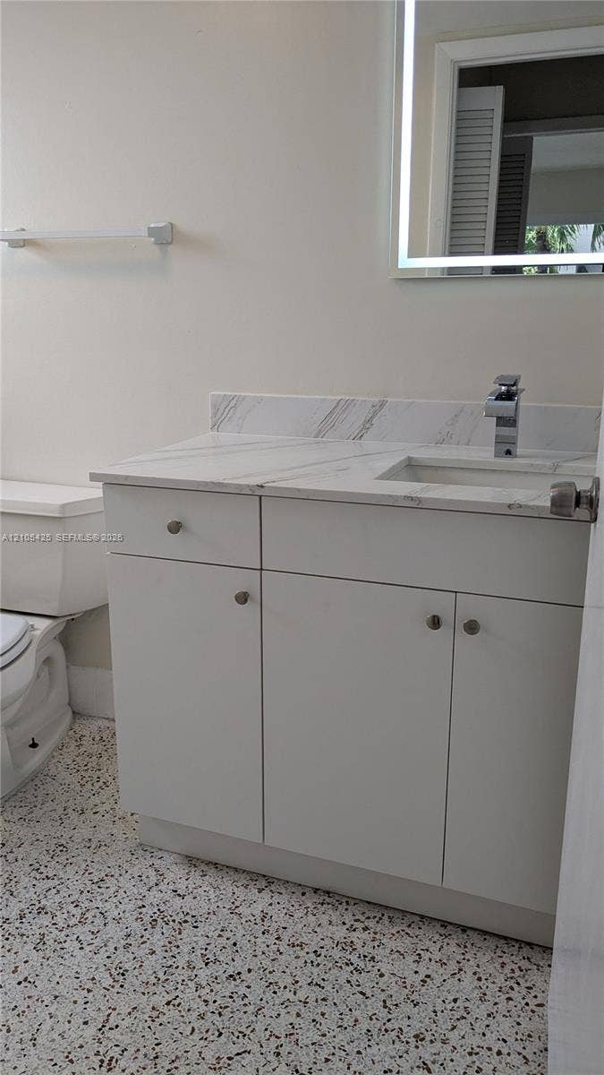White vanity with a light-toned countertop, integrated sink, and a framed mirror with integrated lighting