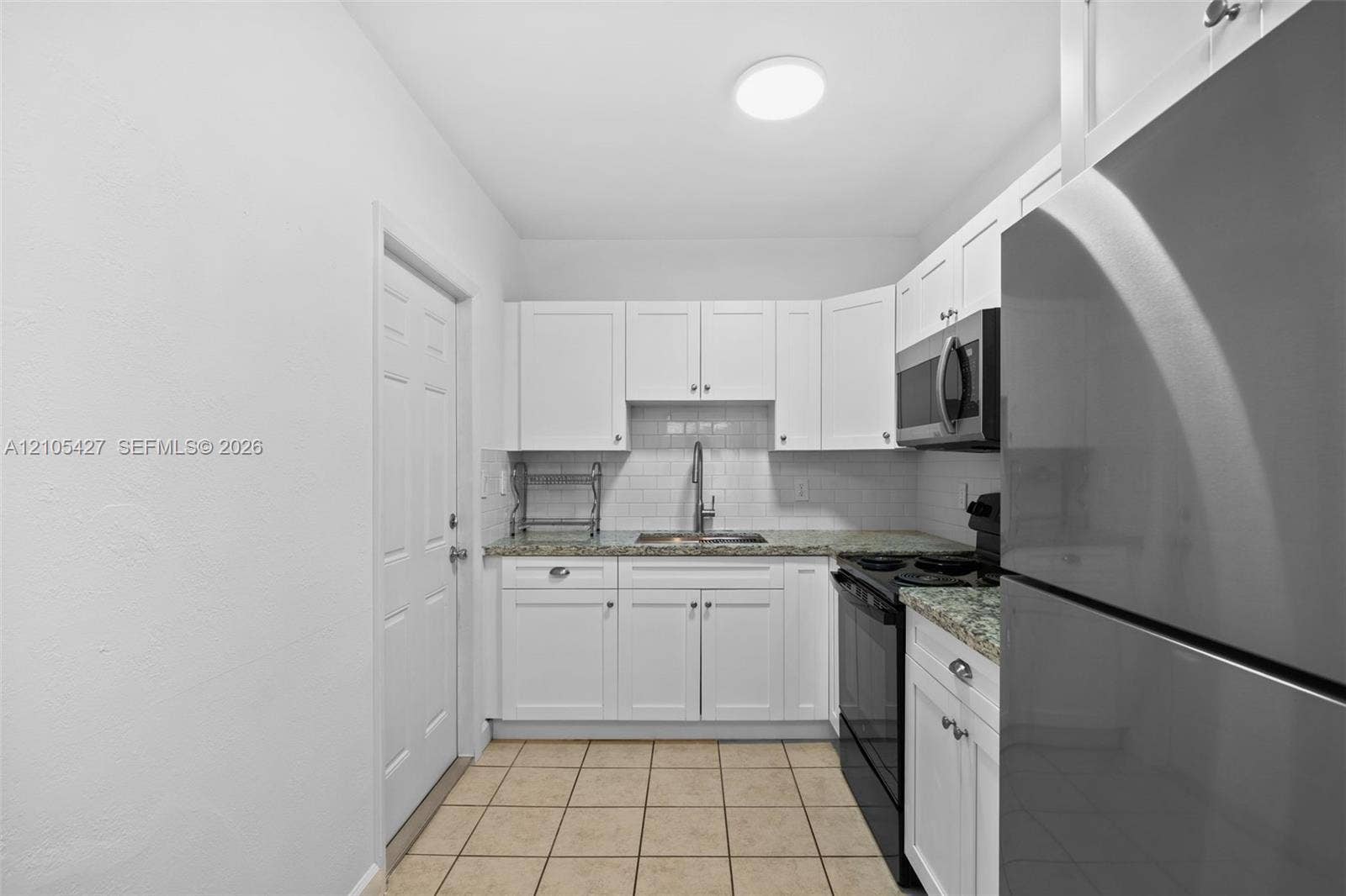 White cabinetry, subway tile backsplash, granite countertops, and stainless steel appliances
