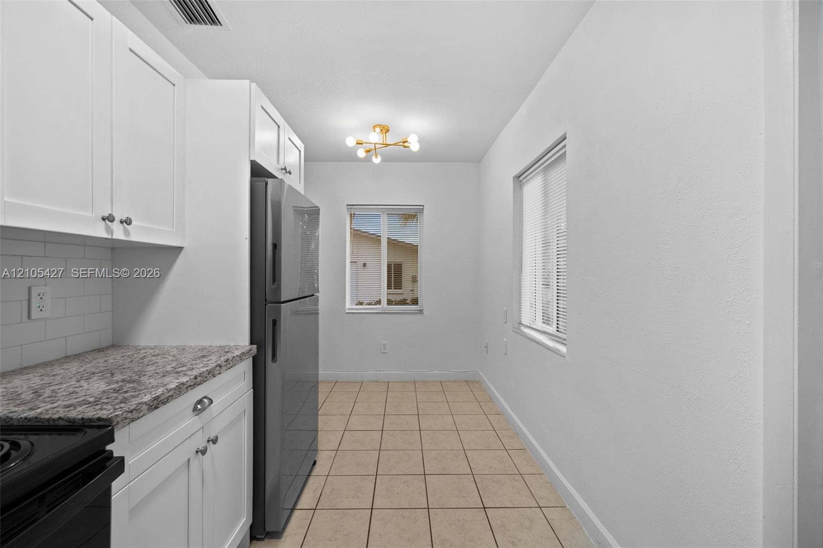 White shaker cabinetry, subway tile backsplash, stainless steel refrigerator, granite-style countertops, and tile flooring
