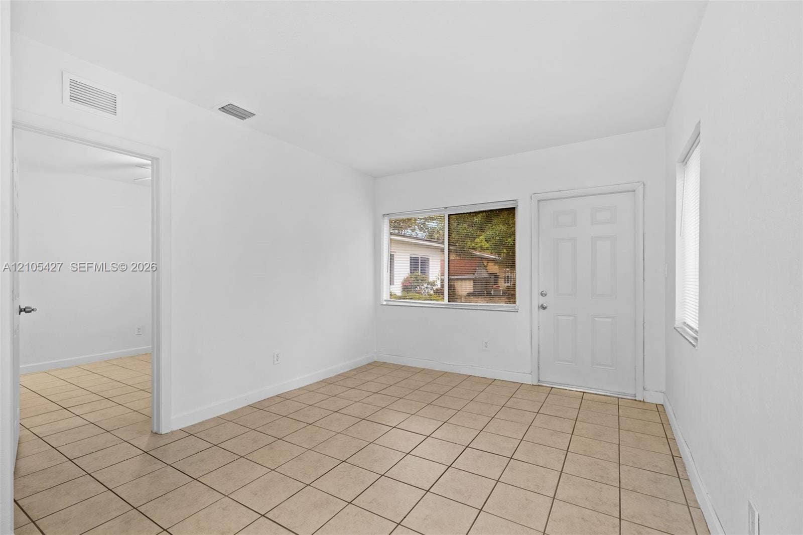 Neutral tile flooring, white interior door, and window with blinds