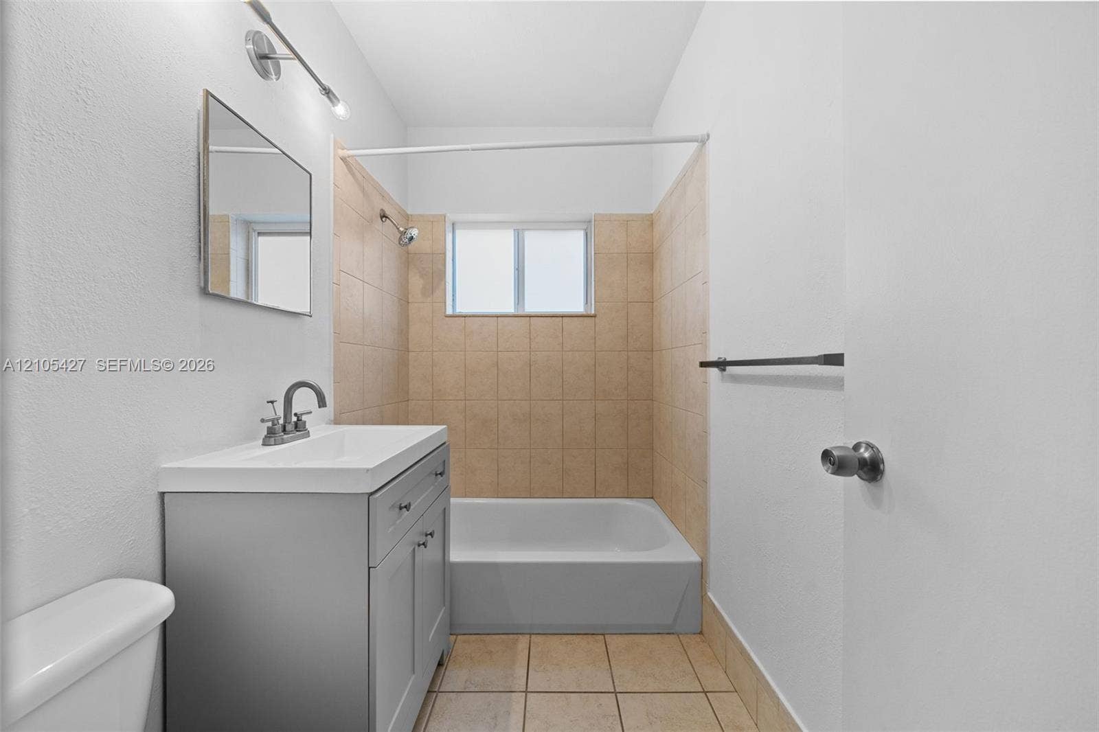 Vanity with integrated sink, rectangular mirror, track lighting, tiled shower surround, and tile flooring