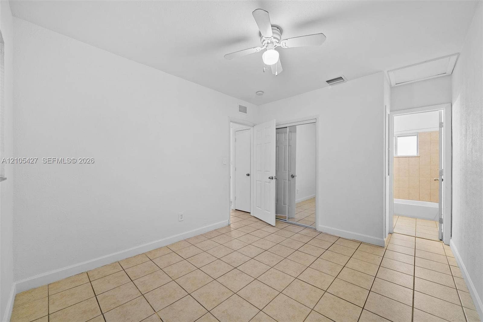 Neutral-toned tile flooring, ceiling fan with light fixture, and white painted walls