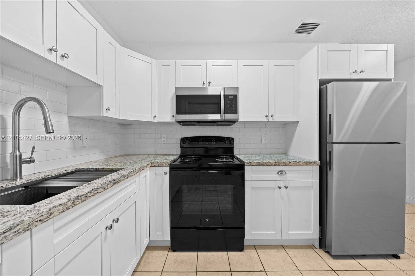 White shaker cabinetry, light-toned countertops, white subway tile backsplash, stainless steel appliances, and tile flooring