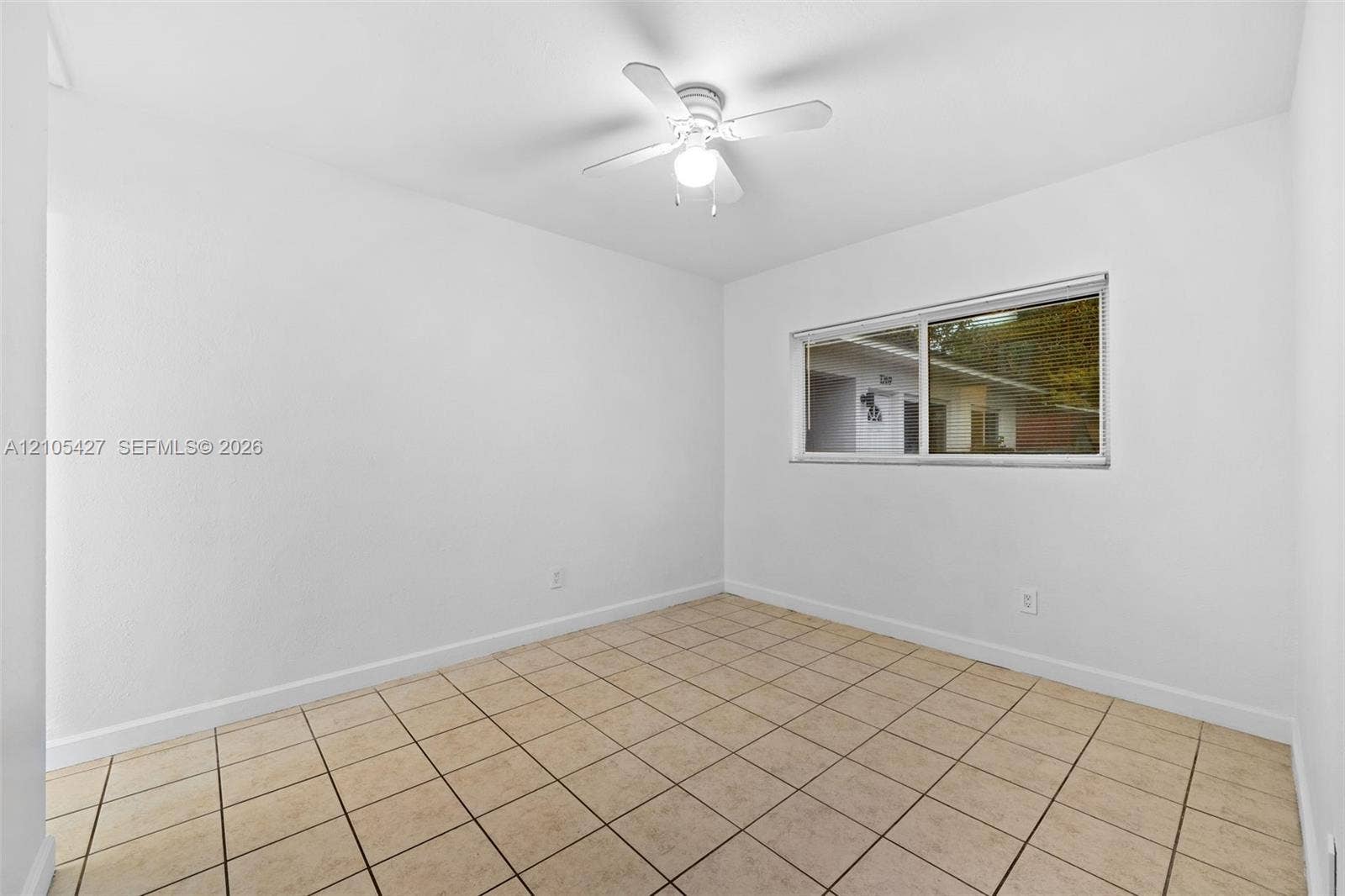 Neutral tile flooring, white ceiling fan with integrated lighting, and a window with horizontal blinds