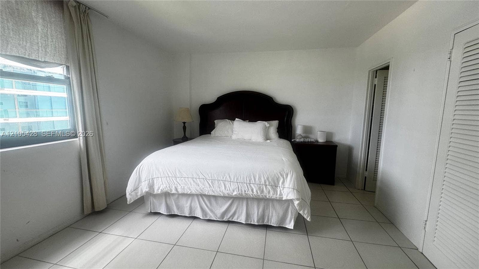 White tile flooring, window with vertical blinds, hinged bifold closet door, and a solid interior door